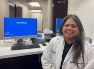 Allied health professional woman smiling while standing in front of medical center computers