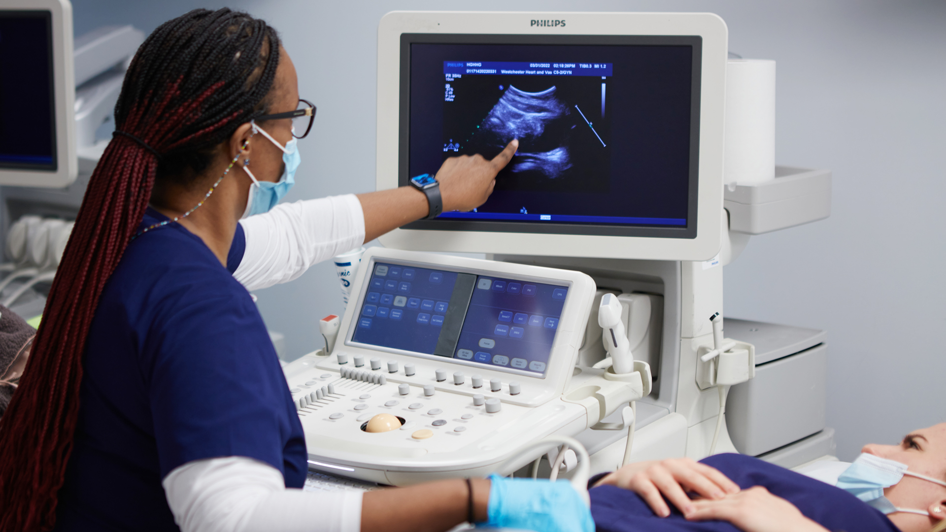 An instructor pointing to a diagnostic medical sonography image while the student as the patient looks on.